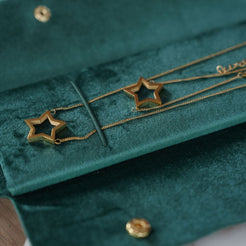Gold star-shaped pendant necklaces displayed on a dark green velvet jewelry box.